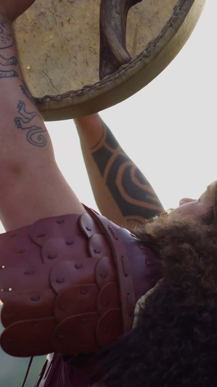 Obese man with long dreadlocks plays shamanic tambourine praying against hills closeup. Musical performance at Altai highland. Traditional instrument