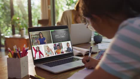 Schoolgirl-using-laptop-for-online-lesson-at-home,-with-diverse-teacher-and-class-on-screen