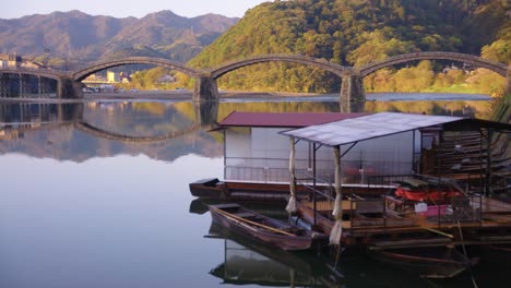 Puente-Arqueado-De-Kintaikyo,-Reflejándose-En-El-Agua-Y-Los-Tradicionales-Barcos-Fluviales.