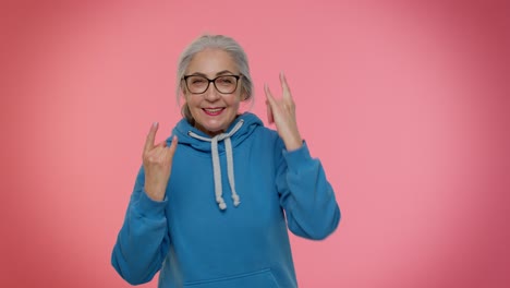 Overjoyed-delighted-crazy-elderly-woman-showing-rock-n-roll-gesture-by-hands,-cool-sign,-dancing