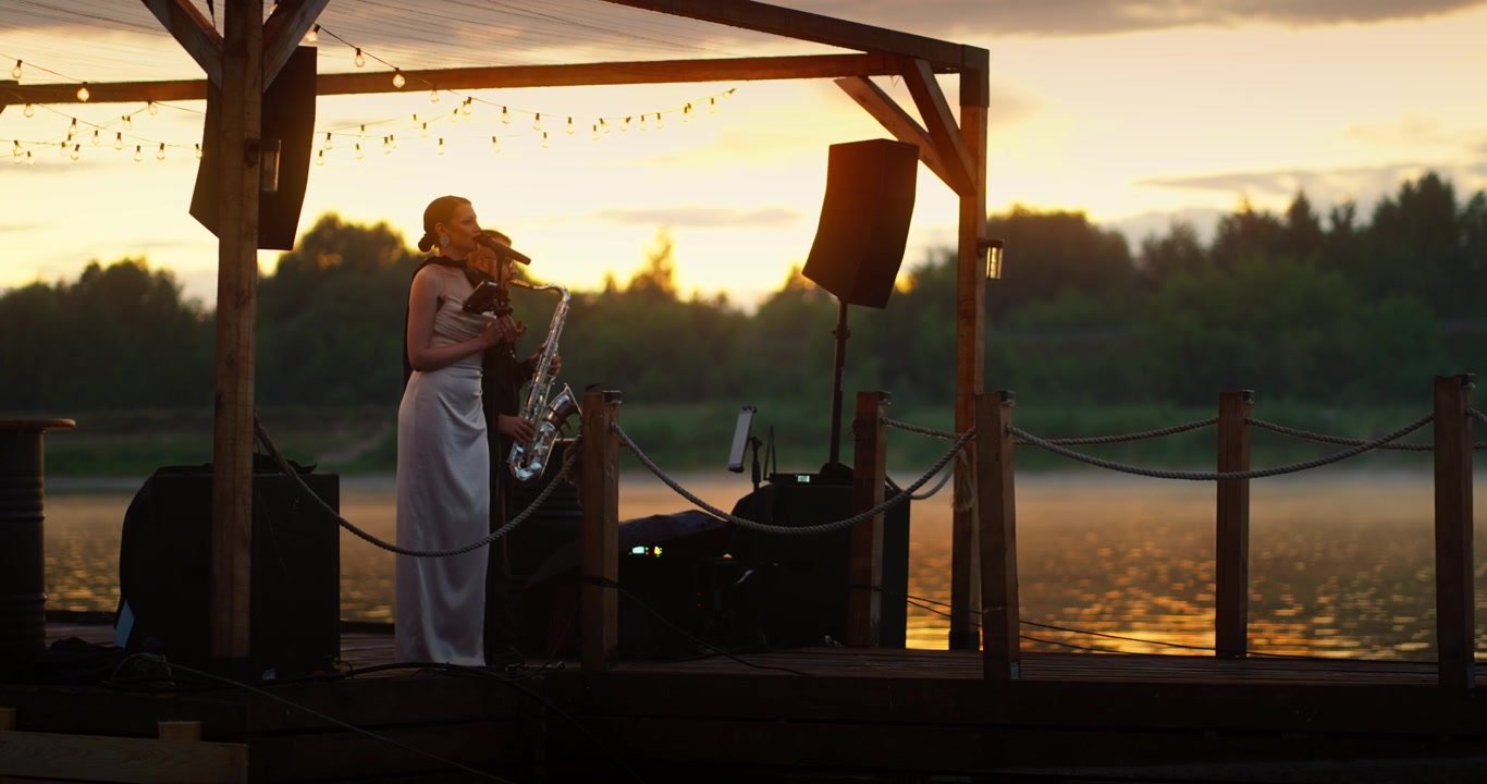 Duo Performing Music on a Lakeside Stage at Sunset