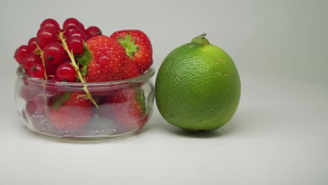 cerezas rojas y fresas dentro del pequeño recipiente transparente con lima afuera girando en el sentido de las agujas del reloj en el plato giratorio - primer plano