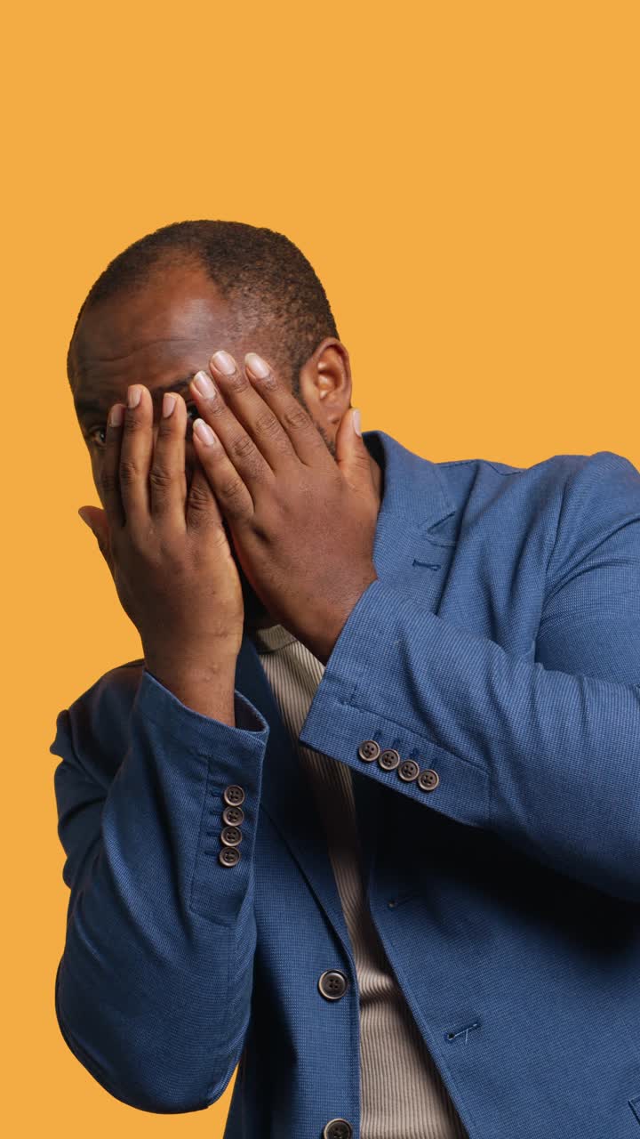 Vertical video Man trembling, covering face in shock watching horror movie, studio background