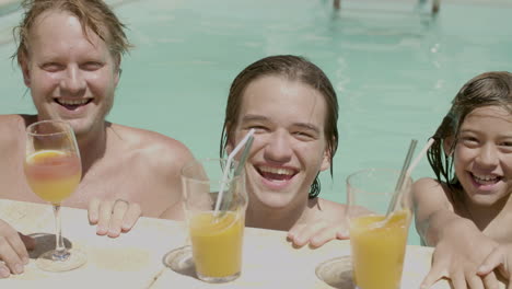 familia feliz en la piscina con sus cócteles junto a la piscina mirando a la cámara y sonriendo