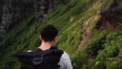 man hikes in tropical forest along cliffside with large backpack, close up