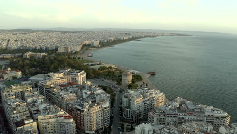 cinematic smooth aerial drone shot looking out to sea with the city of thessaloniki in view at sunset with the white tower of thessaloniki in the middle, greece in 4k