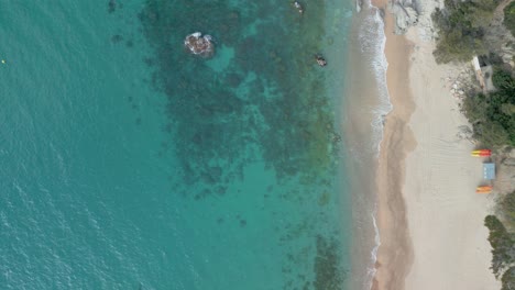 Overhead-shot-of-a-tropical-beach-with-transparent-turquoise-sea-green-vegetation-and-rocks-taken-from-the-air