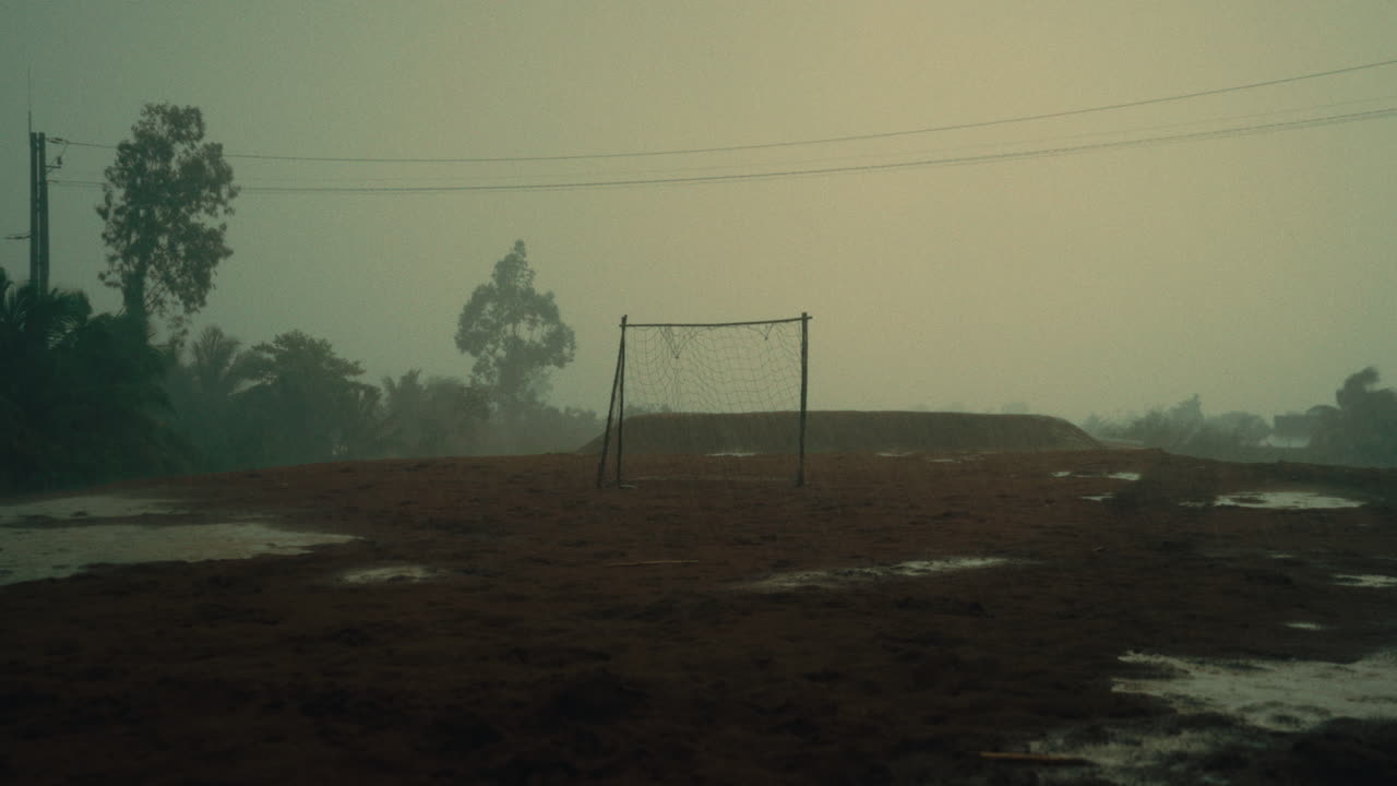 Campo da calcio bagnato con porta vuota, tempo nebbioso e pozzanghere dopo la pioggia
