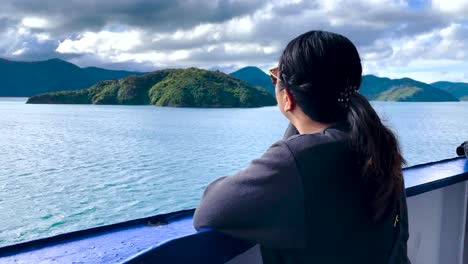 dark haired woman lost in thought stares from boat out at islands and blue bay waters in new zealand