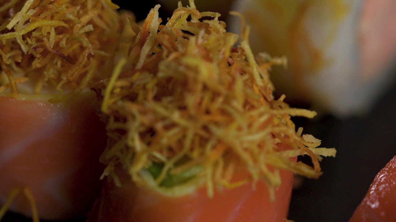 Chef che aggiunge una guarnizione croccante di patata dolce su sushi di salmone, primo piano.