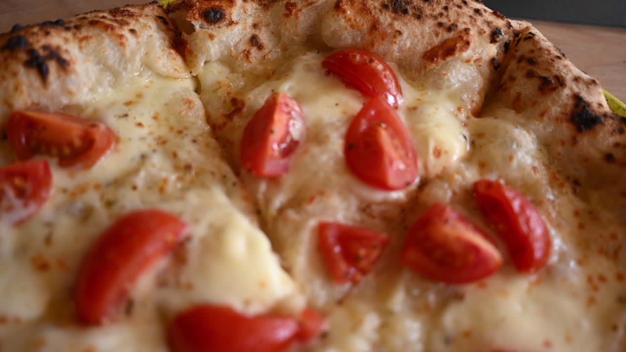 Primo piano di pizza appena sfornata, guarnita con formaggio fuso e pomodorini