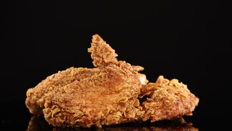 a hand reaches in and lifts a crispy fried chicken wing from a pile, shot in slow motion with dramatic studio lighting against a black background
