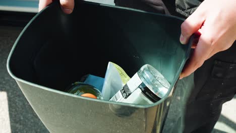 a middle age man cleans out his work vehicle of bottles and wrappers using a black plastic garbage can