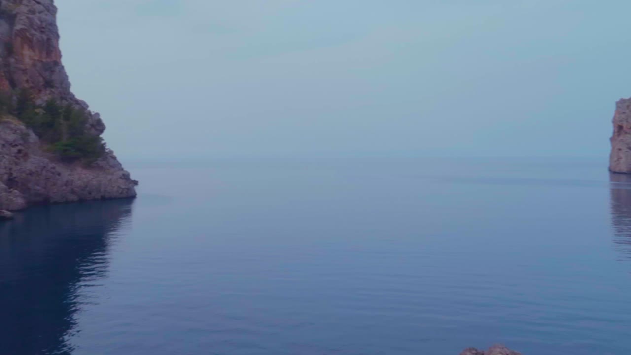 고요한 푸른 물, 말로르카(malorca)가 있는 흐린 하늘 아래 석회암 산으로 둘러싸인 발레릭 섬(baleric island)의 매혹적인 저녁 패닝 전망