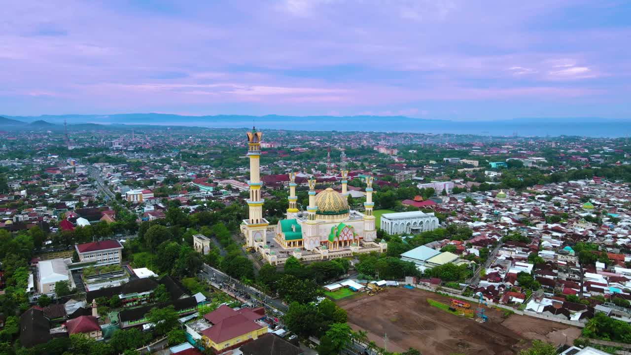 Masjid Kuning (Masjid Habbul Wathan) di Indonesia, pemandangan udara drone saat hari cerah dengan langit biru dan matahari terbenam. Terletak di pusat kota Indonesia, masjid ini adalah salah satu masjid terindah di dunia.