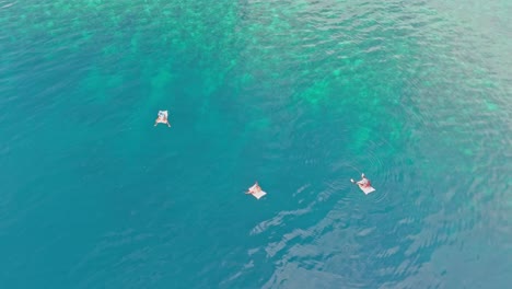 three people floating individually in the deep blue sea of dinagat islands using inflatable sacks.