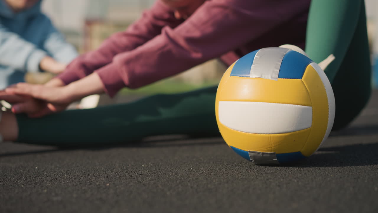 primer plano de voleibol cerca de una dama estirándose con otras damas en el fondo haciendo ejercicio en una arena deportiva al aire libre, mostrando fitness, trabajo en equipo y atletismo