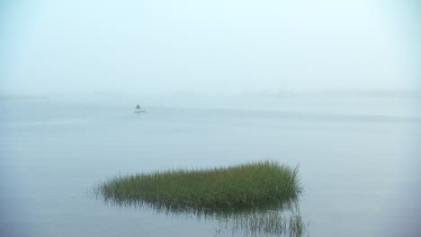 wide shot of man rowing a row boat into the eerie maine fog