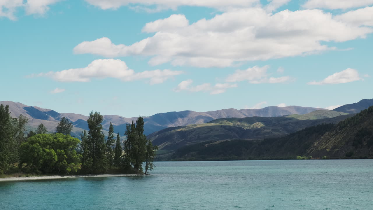 una vista panorámica de un tranquilo lago azul con montañas distantes bajo un cielo parcialmente nublado