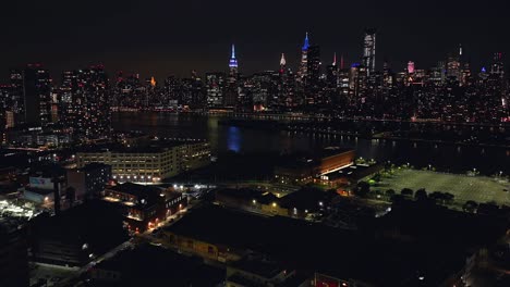 Un-Lapso-De-Tiempo-Aéreo-Por-La-Noche-Sobre-Long-Island-City,-Queens-Con-El-Lado-Este-De-La-Ciudad-De-Nueva-York-Al-Fondo