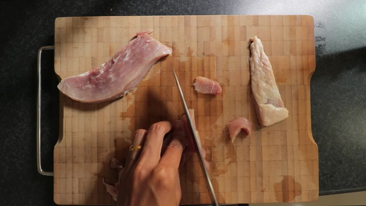 rebanar cuidadosamente la carne de cerdo cruda en una tabla de cortar de bambú con un cuchillo de chef de acero inoxidable - vista superior