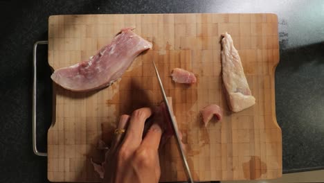 Carefully-slicingr-raw-pork-meat-on-a-bamboo-chopping-board-with-a-stainless-steel-chef-knife---Top-view