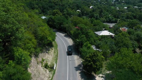 a black suv driving alone on the asphalt road in the mountain with lush trees in racha, georgia on a fine weather - aerial