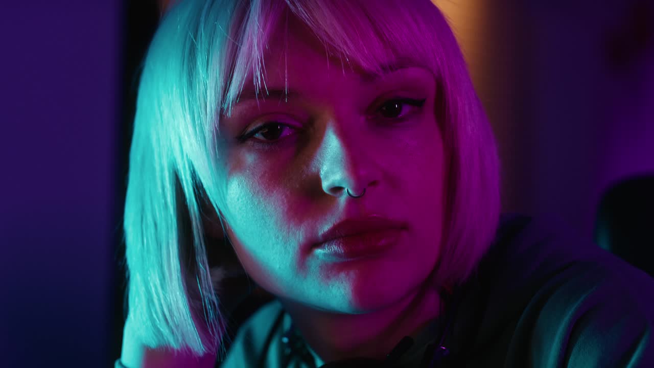 mujer caucásica joven seria navegando por el teléfono móvil mientras un descanso durante el juego por la noche en la computadora de escritorio