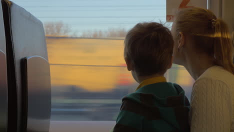 small boy with mother sitting against window in their rail train place and watching outside on freight trains