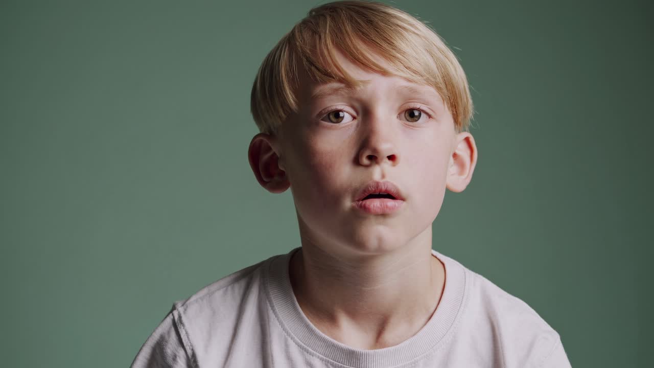 A close-up video shot of a young boy with a thoughtful expression against a green background