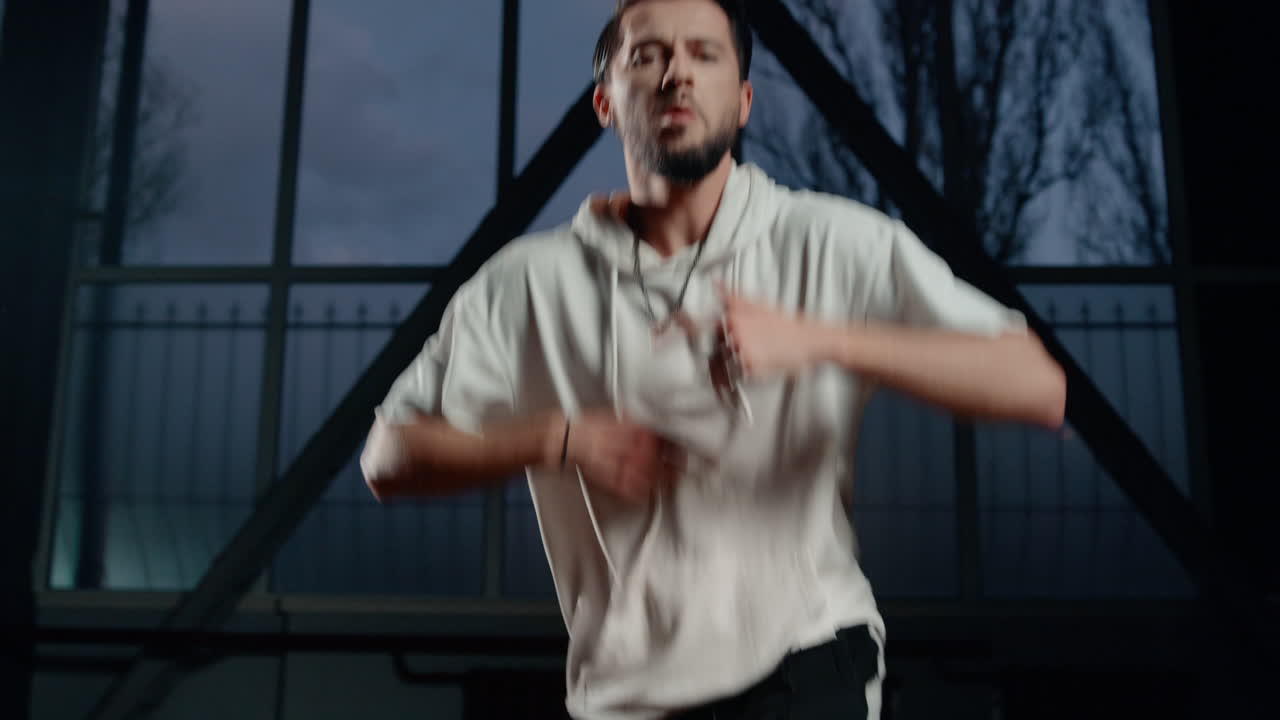 Confident man having dance workout in dark class. Guy dancing hip hop indoors.