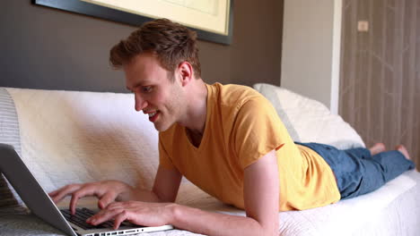 young man lying on bed using laptop