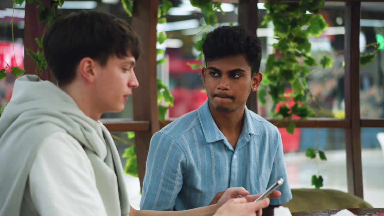 Two teenagers discussing content seen on phone while looking away from device sharing surprised and amused expressions, in beautiful but casual indoor setting peer conversation about viral video