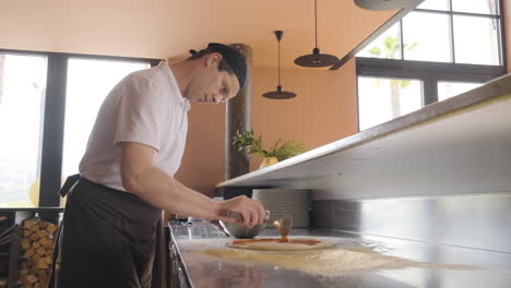 side view of a chef spreading sauce on pizza dough on a restaurant kitchen countertop