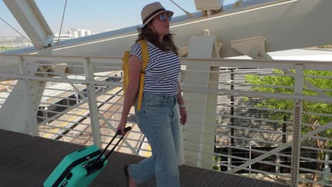 a woman is walking with a green suitcase on a bridge