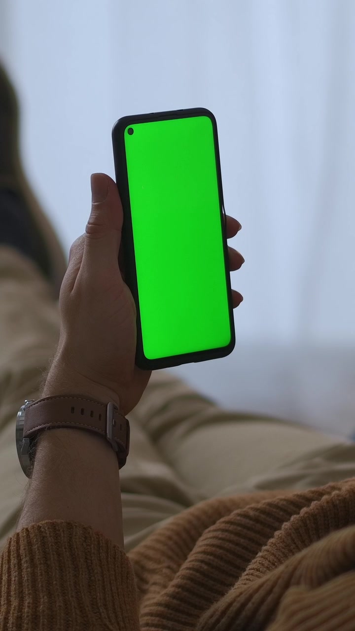 Persona che tiene uno smartphone con schermo verde mentre si rilassa
