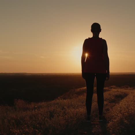 slender woman stands on a hill in the rays of the setting sun