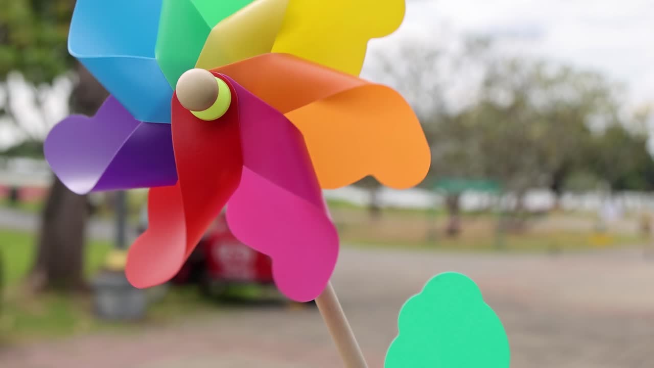 A colorful pinwheel spins against a blurred park background, showcasing dynamic motion and vibrant hues.
