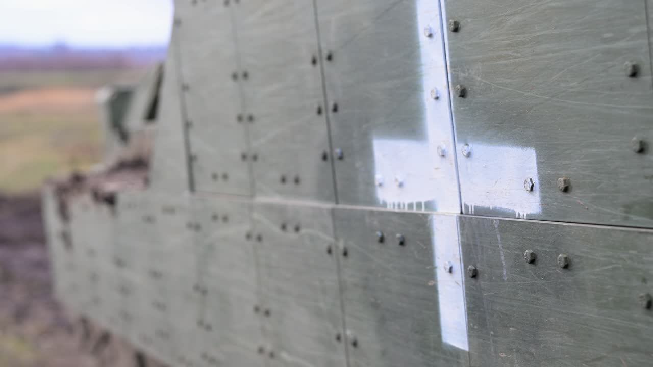A close-up of a white cross stenciled on the side of an M2 Bradley IFV in Ukraine. This marking designates the fighting vehicle for a life-saving casualty evacuation (CASEVAC) role