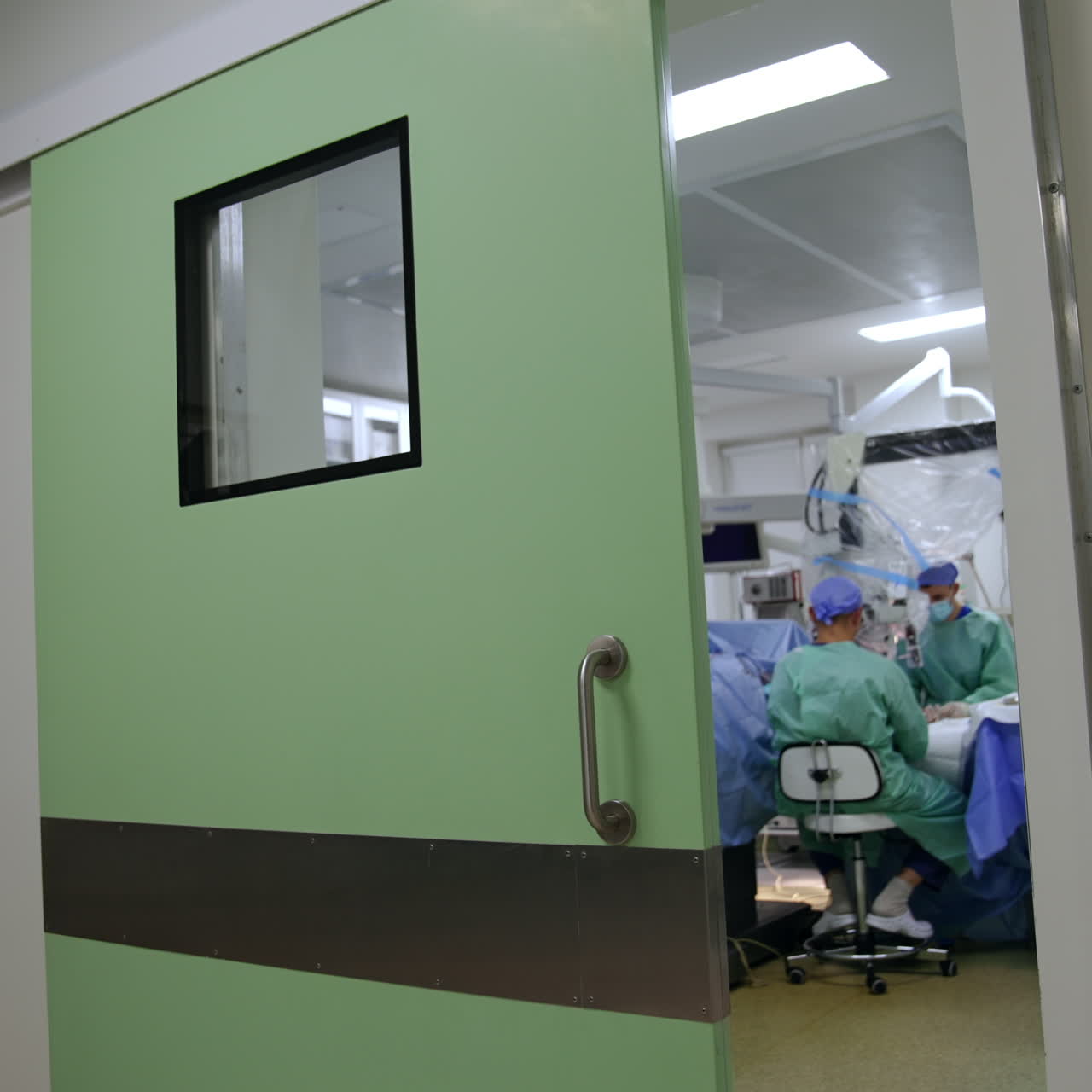 Imagens no corredor do hospital perto da sala cirúrgica. Cirurgião realiza operação olhando para o microscópio.