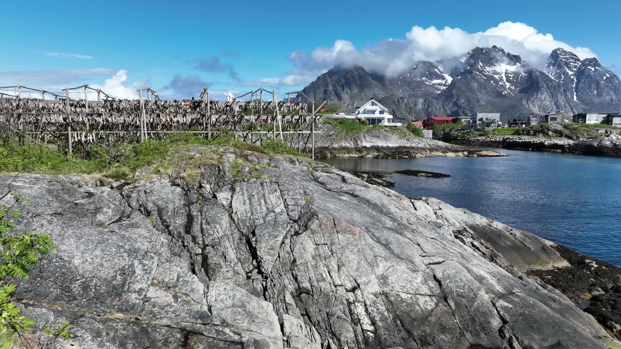 Low flyover above rocky coastline of Lofoten Islands toward traditional wooden fish drying racks, Norway