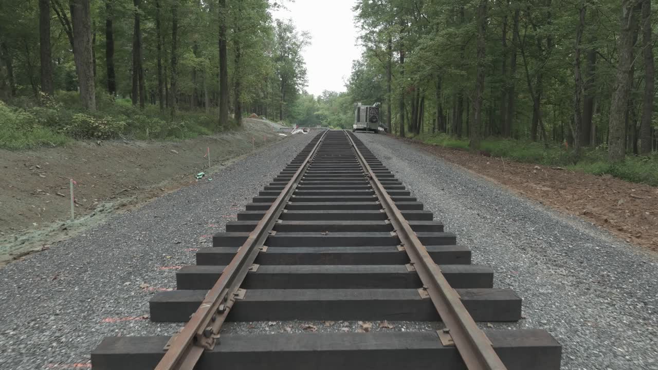 View of train tracks running through a forested area. The path shows different conditions and updates along the track. The environment has trees and gravel surroundings