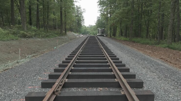 View of train tracks running through a forested area. The path shows different conditions and updates along the track. The environment has trees and gravel surroundings