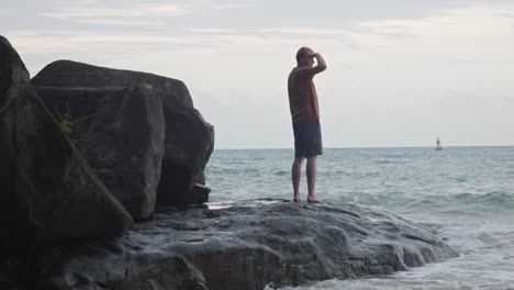 Mann-Blickt-Auf-Das-Meer,-Während-Er-Auf-Einem-Felsen-Am-Strand-Von-Dam-Trau,-Vietnam,-Steht