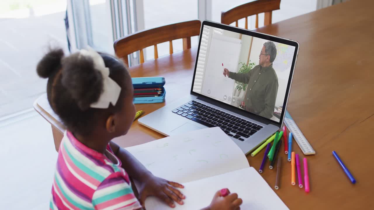 African american girl doing homework while having video call with male teacher on laptop at home
