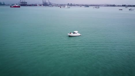 Weißes-Boot-Friedlich-Verankert-In-Ruhigem-Blauem-Wasser,-Hafen-Im-Hintergrund,-Callao,-Peru