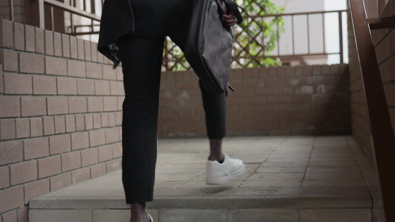 Camera follows individual in white sneakers climbing staircase indoors, steps steady, casual denim and hoodie style, modern building lighting, focus on footwear and movement, upward commute vibe