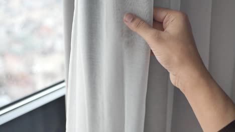 persona abriendo una cortina blanca por una ventana