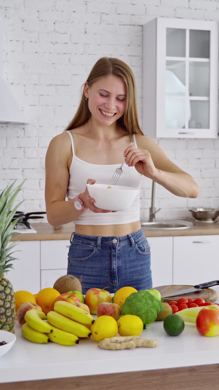 Woman with fresh salad in the kitchen. Attractive girl eating organic food at home. Beautiful housewife cooking salad. Healthy lifestyle. Vertical video