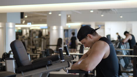 fit man taking deep beath relaxing leaning on parallel bars after doing dips workout training in gym - profile view slow motion